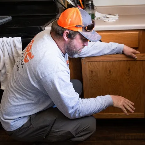 Agro Employee inspecting for pests under a kitchen sink.